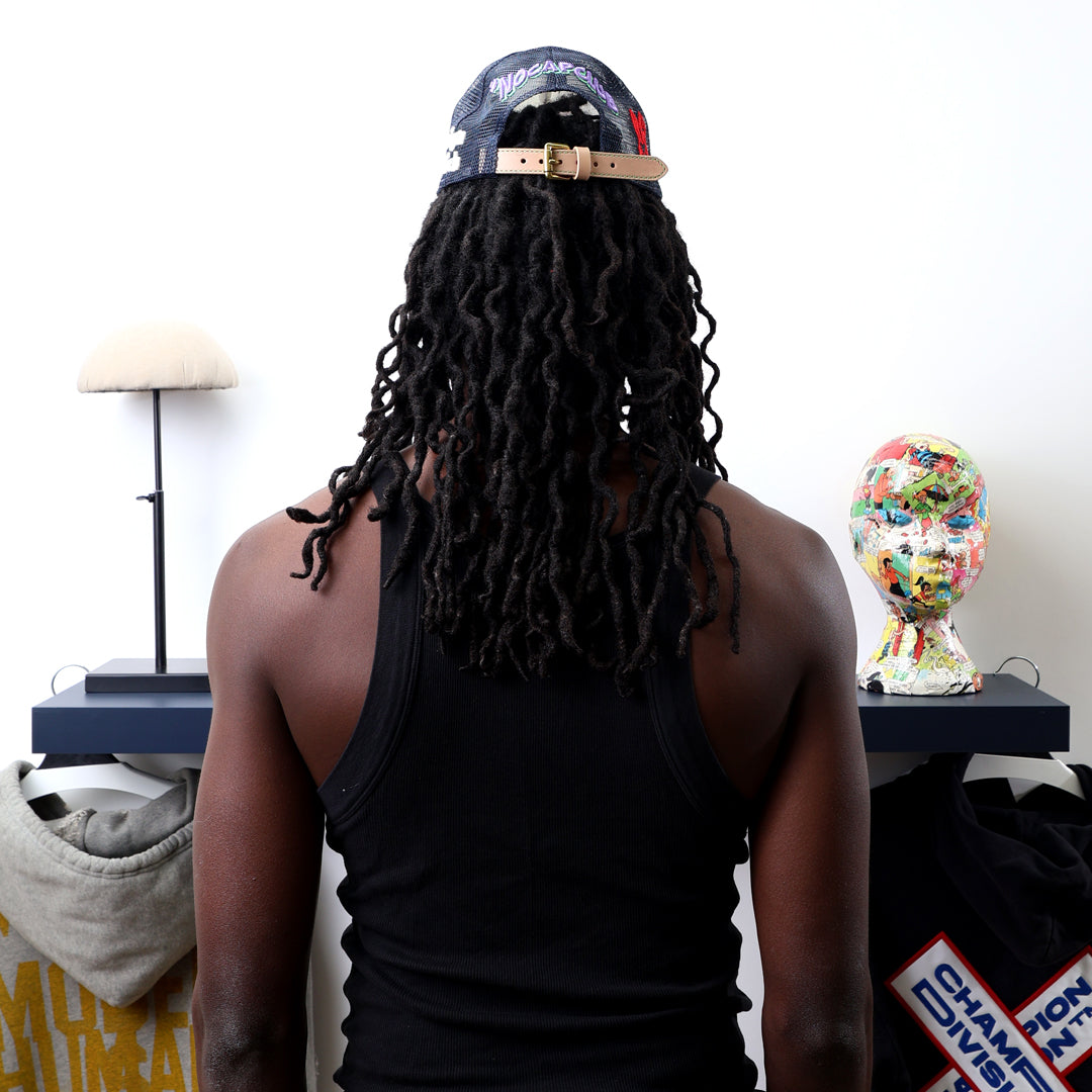 Person with dreadlocks, cap, facing art pieces on shelves.