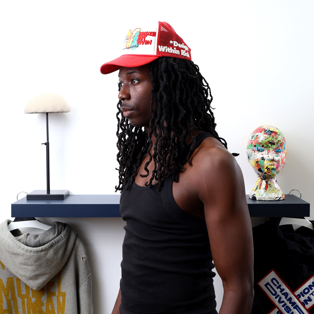 Man in red cap, black tank top, near shelf.