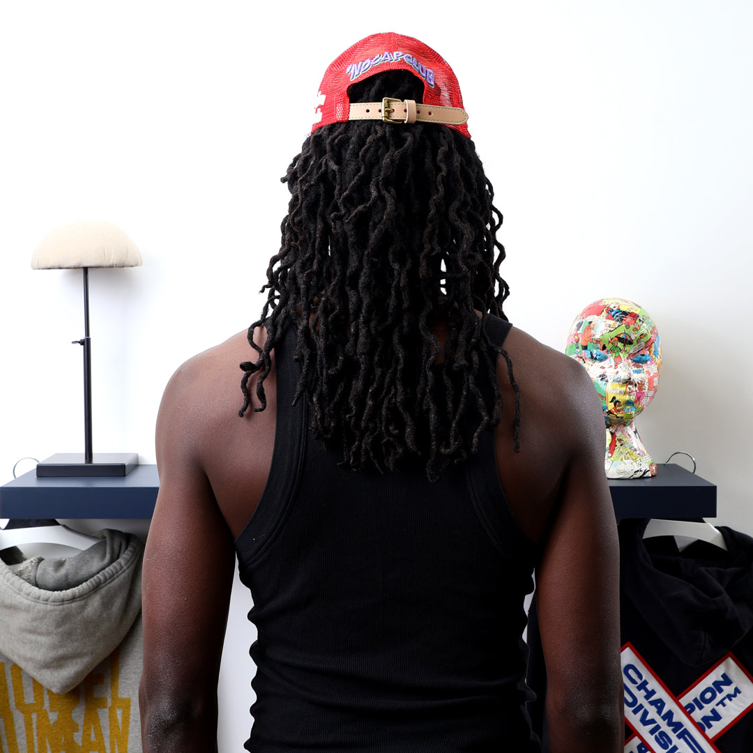 Man with dreadlocks, red cap, facing art pieces.