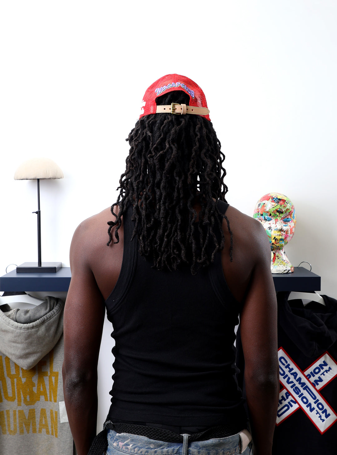 Man with dreadlocks, red cap, facing art pieces.