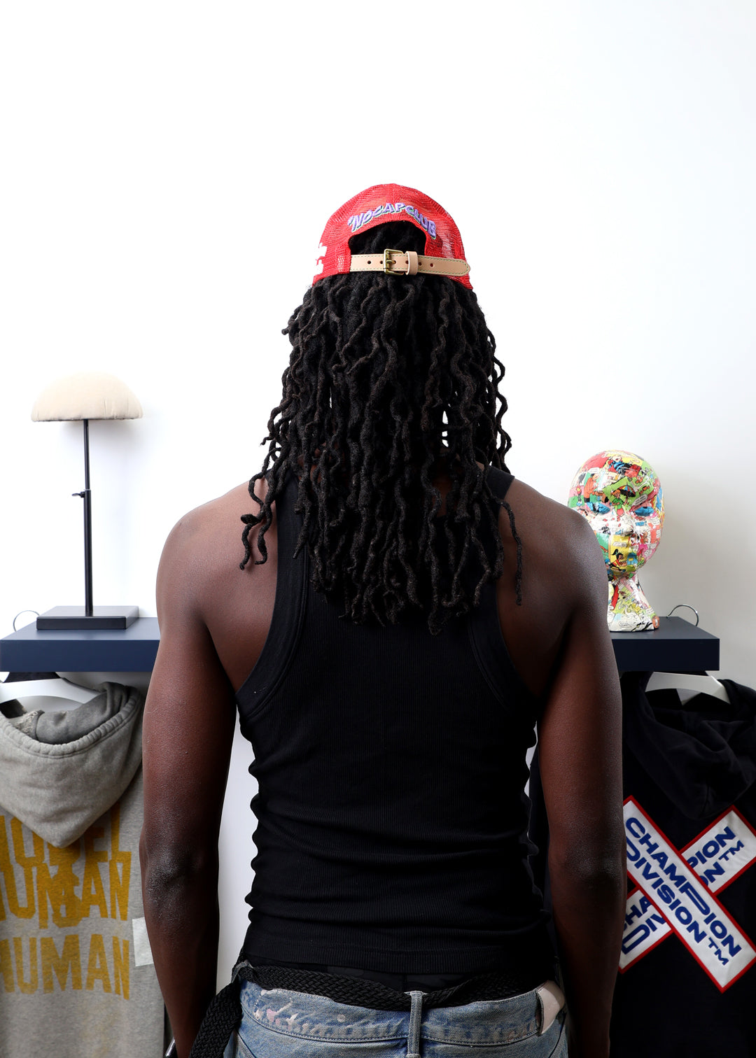 Man with dreadlocks, red cap, facing art pieces.