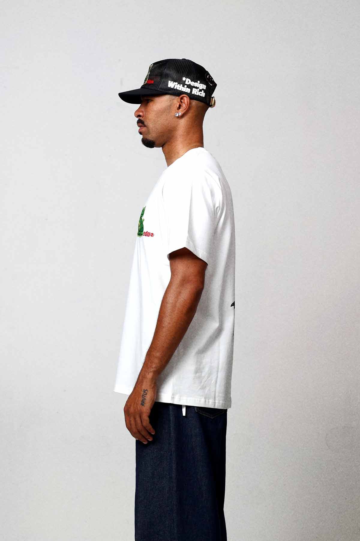 Man in white t-shirt and cap, side view.