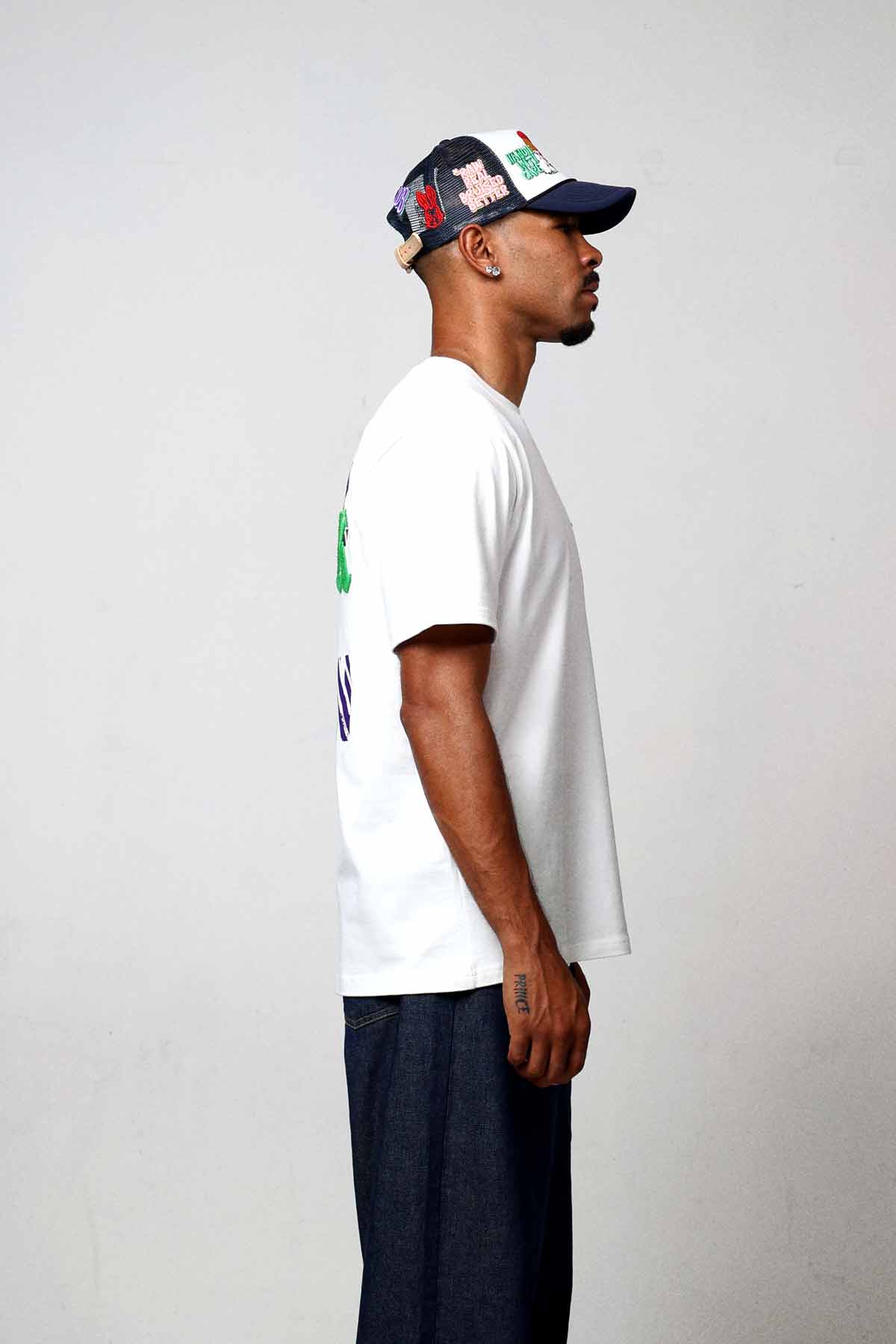 Man in white t-shirt and cap, side view.