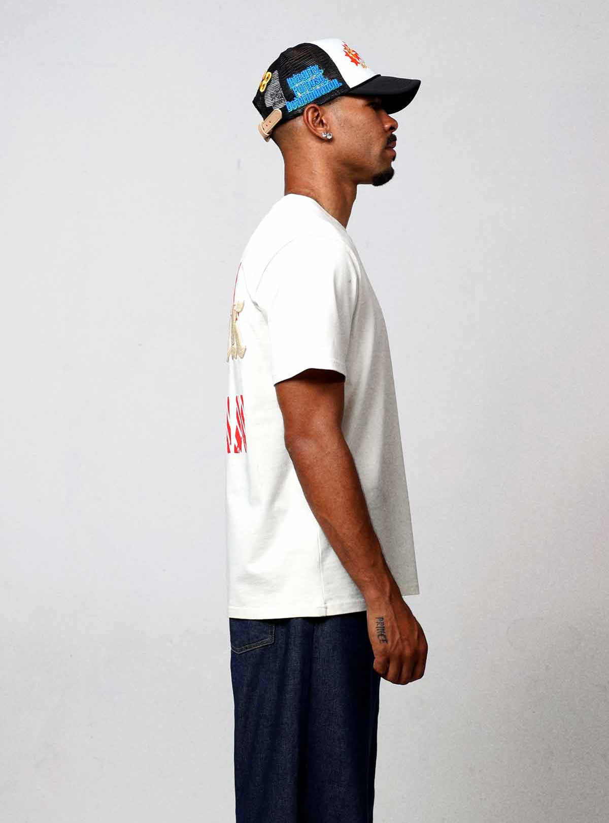 Man in white t-shirt and cap, side view.