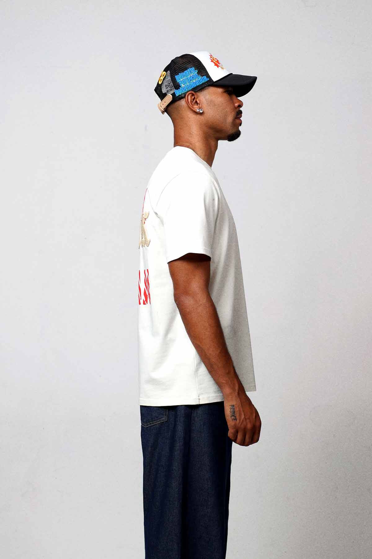 Man in white t-shirt and cap, side view.