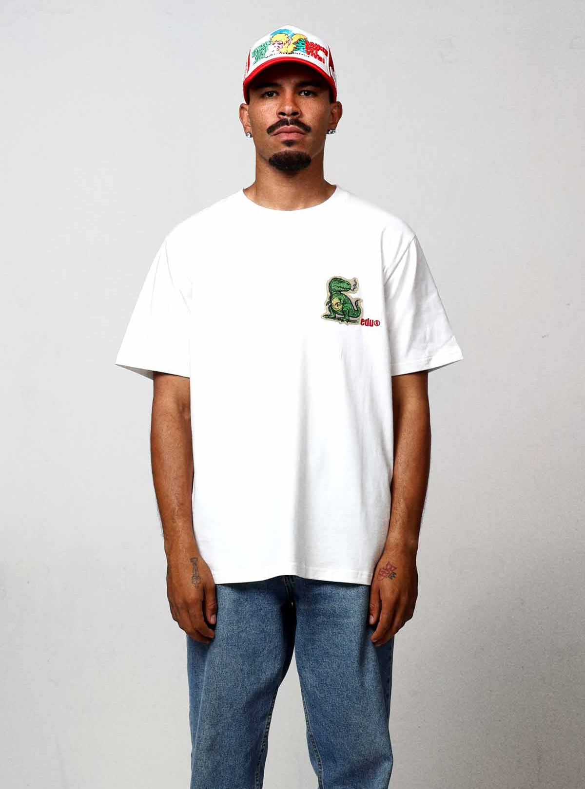 Man in white t-shirt and jeans, wearing a cap.