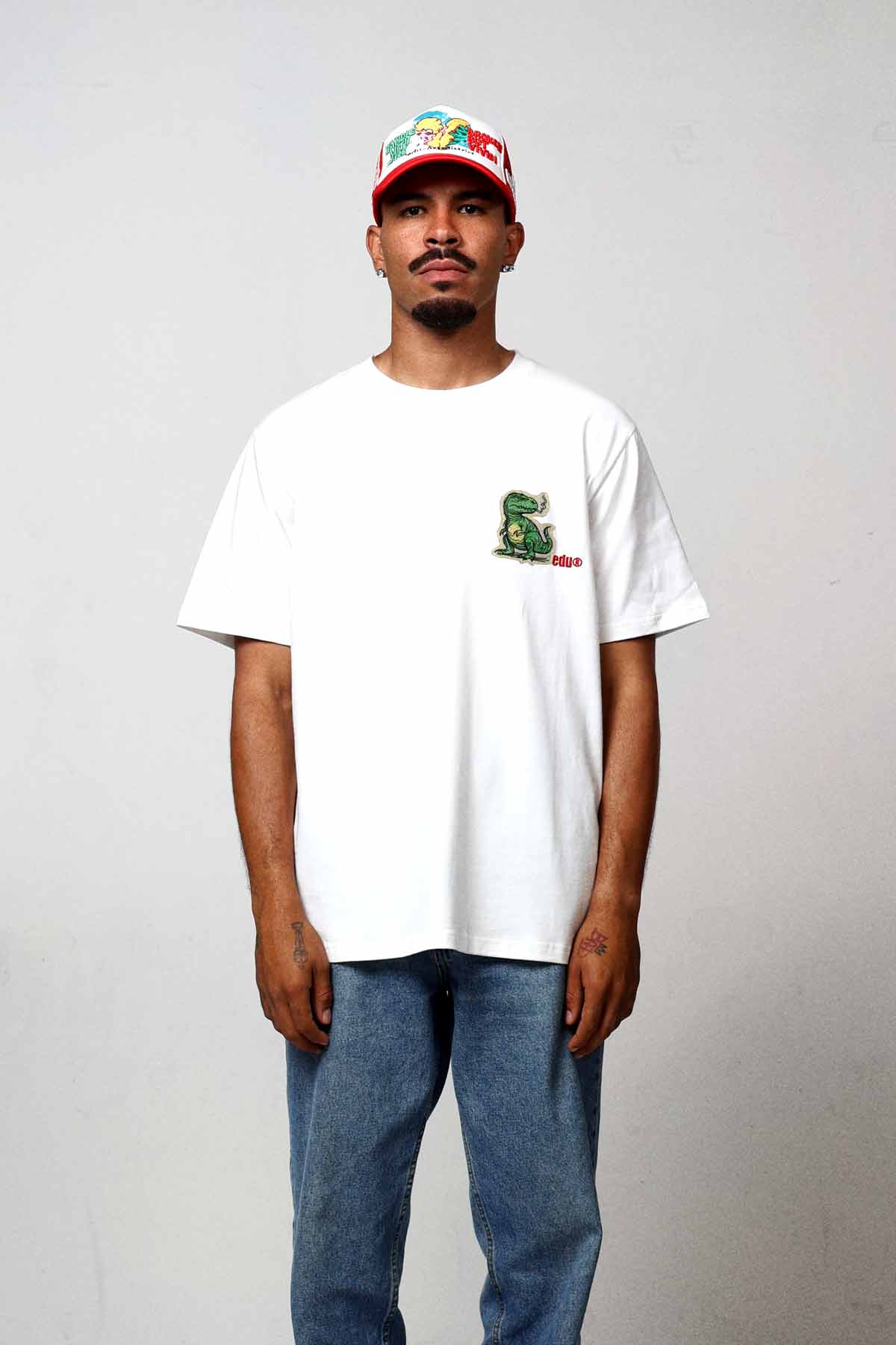 Man in white t-shirt and jeans, wearing a cap.