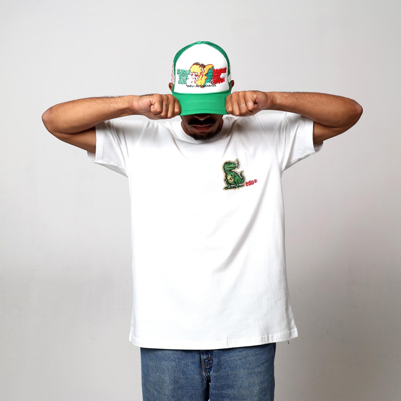 Man in white t-shirt, cap, covering face with hands.