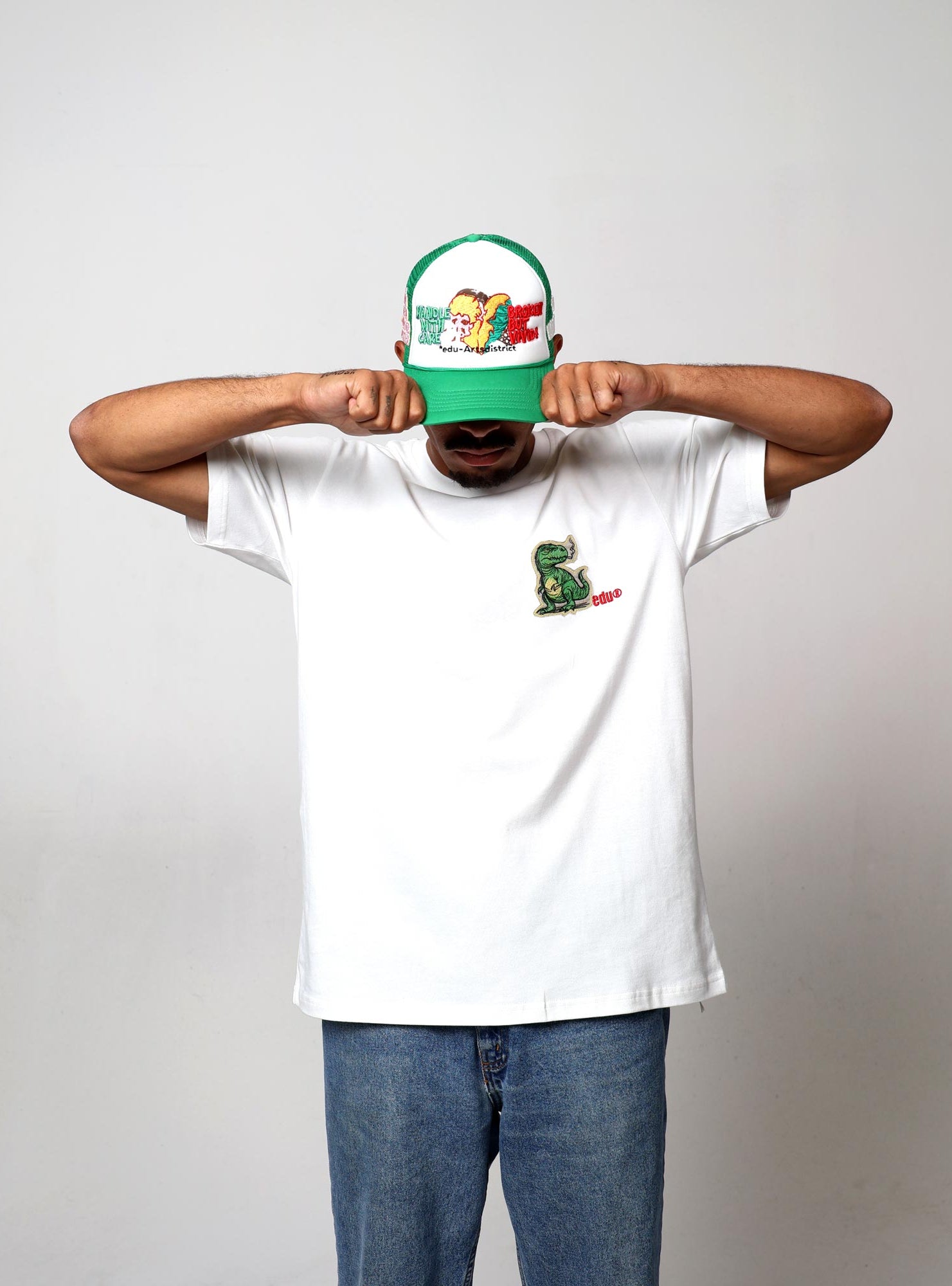 Man in white t-shirt, cap, covering face with hands.