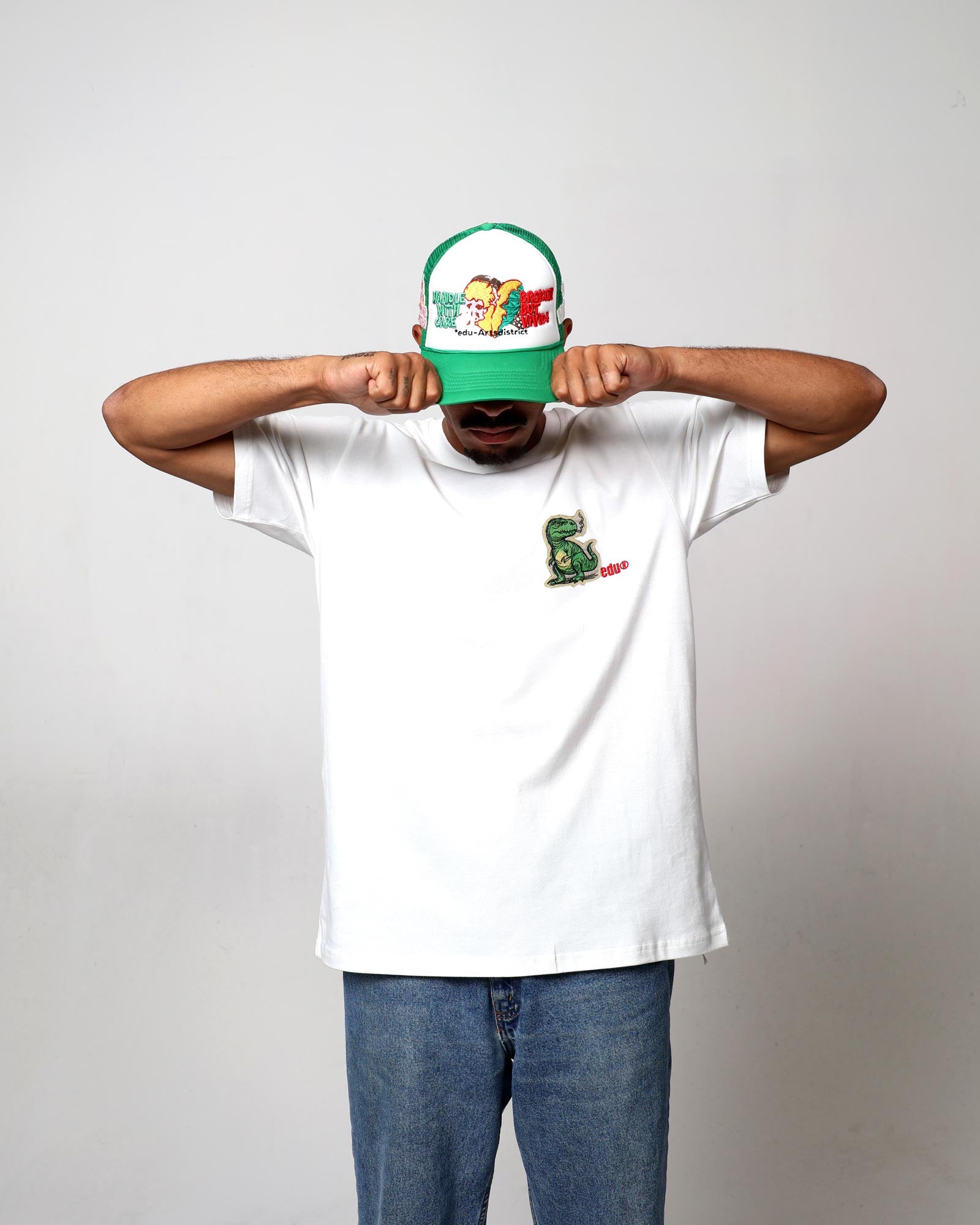 Man in white t-shirt, cap, covering face with hands.