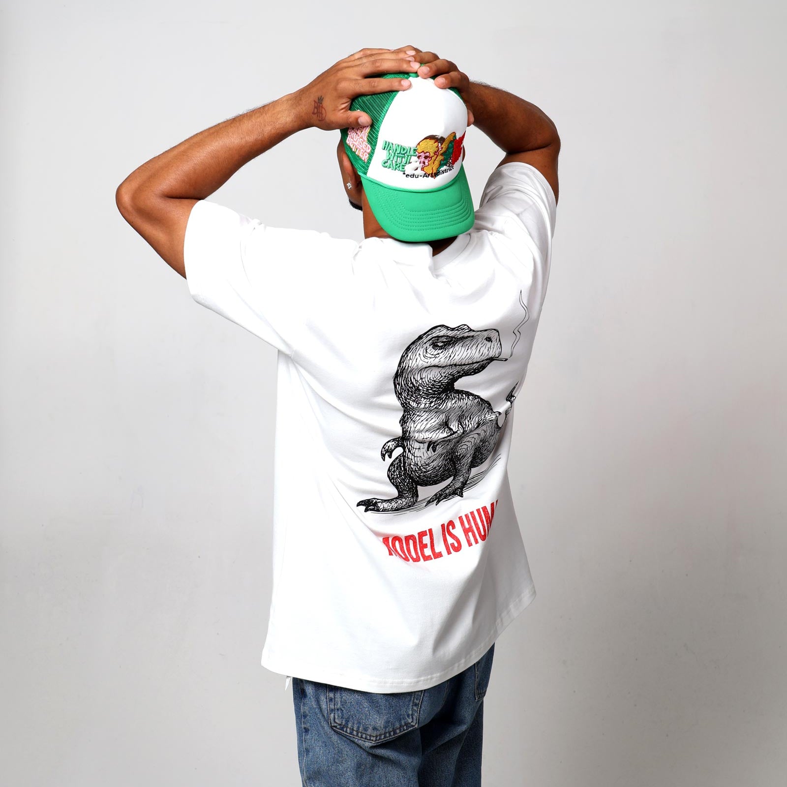 Man in dinosaur t-shirt, green cap, facing away.