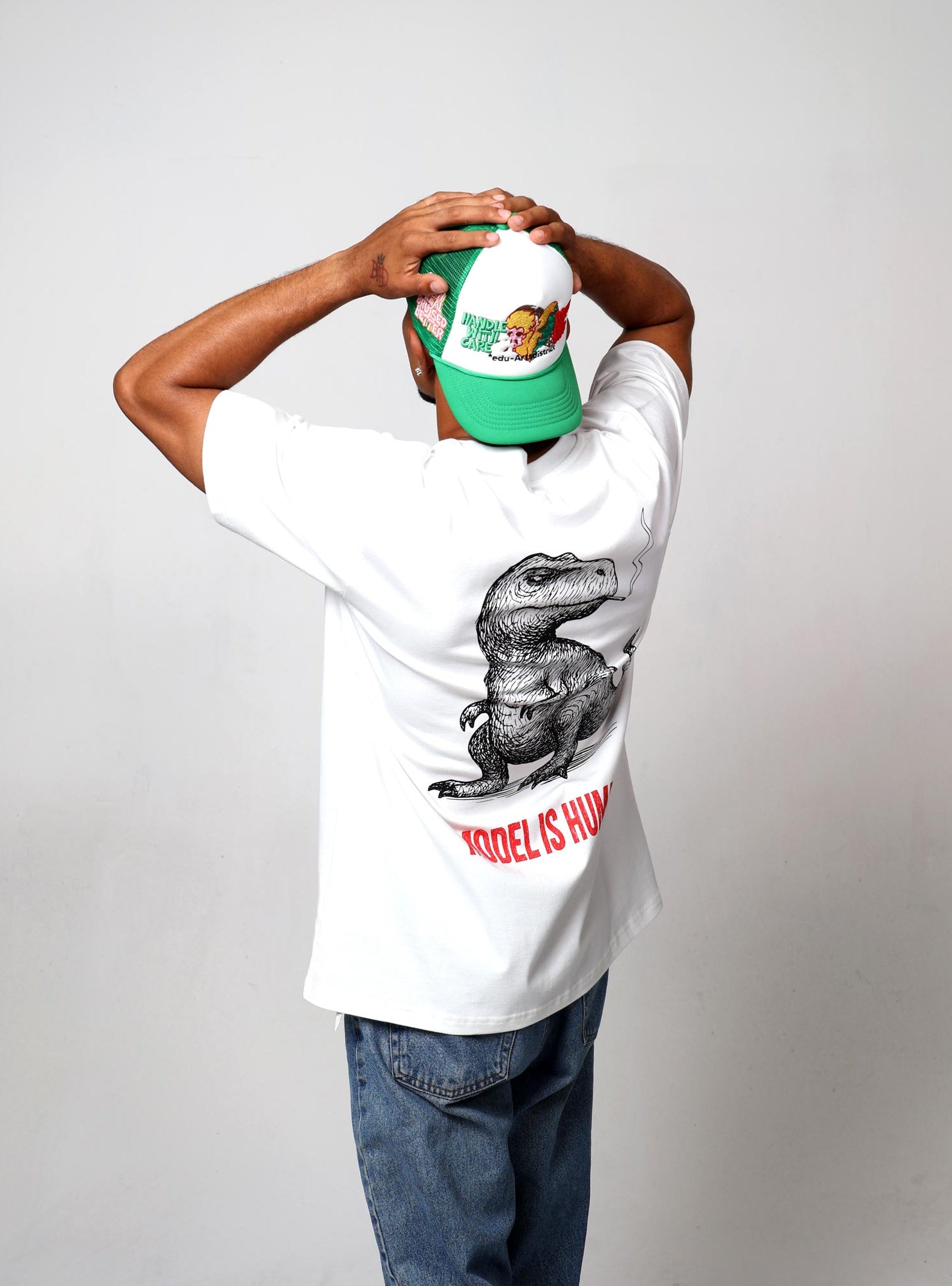 Man in dinosaur t-shirt, green cap, facing away.