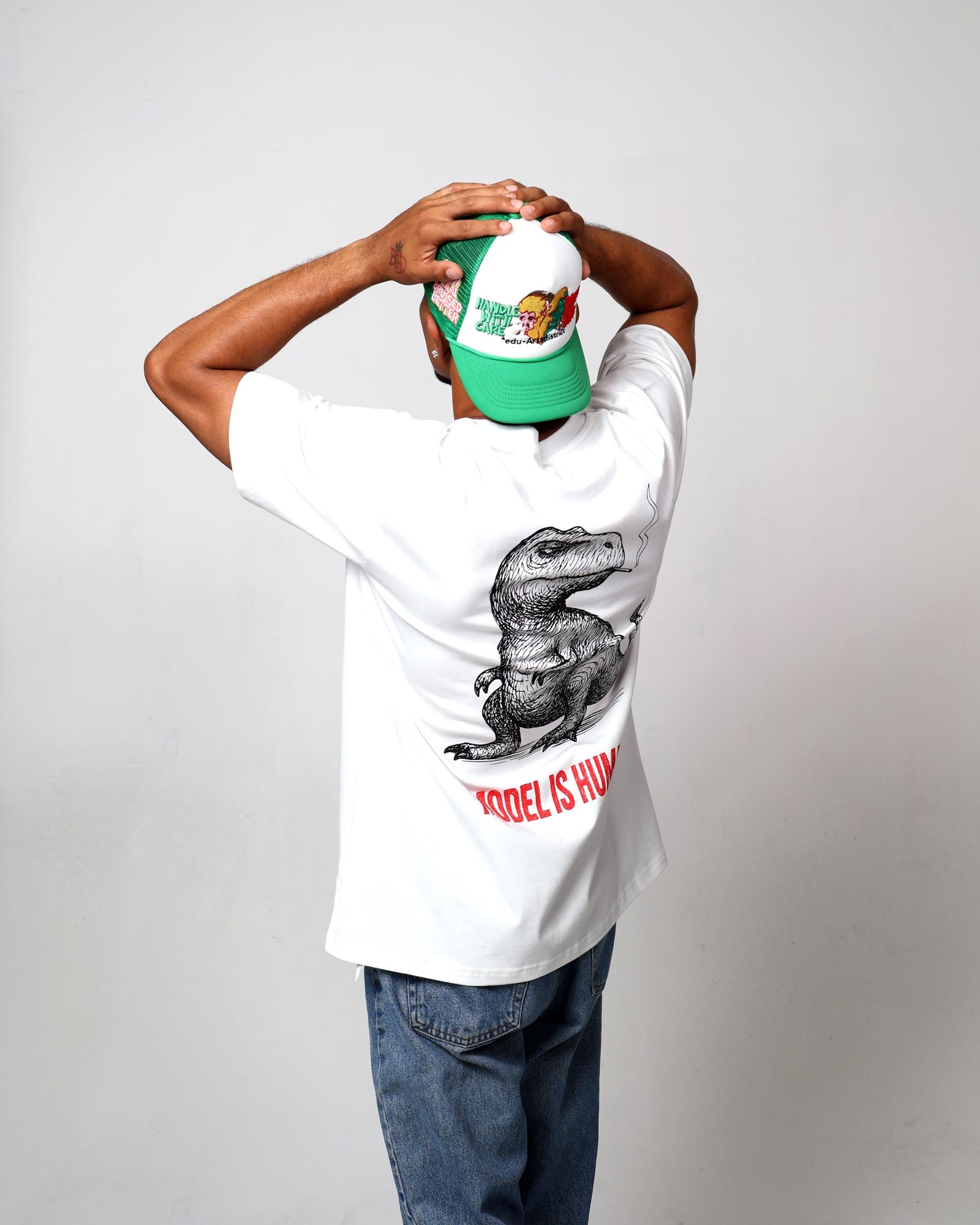 Man in dinosaur t-shirt, green cap, facing away.