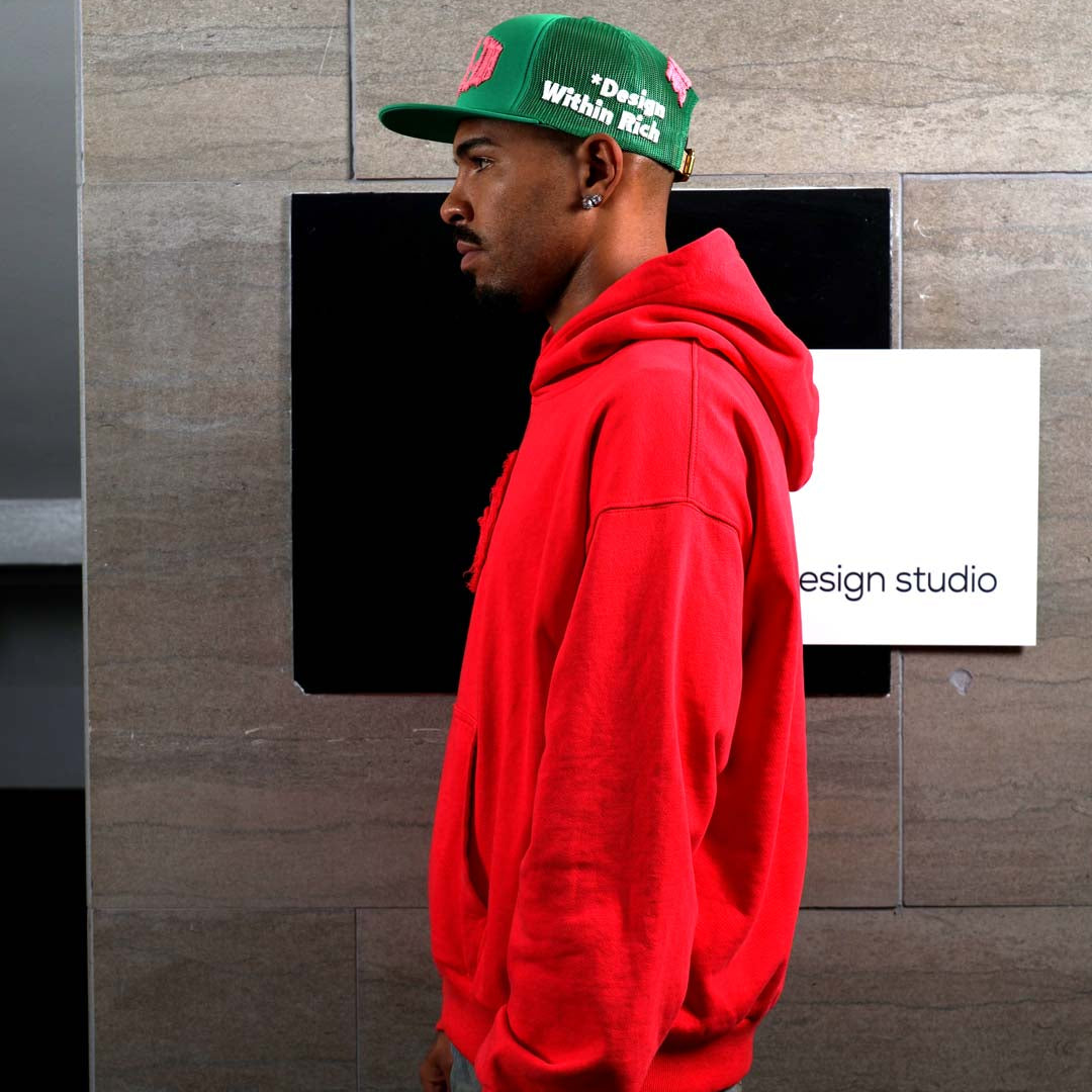 Man in red hoodie and green cap, side profile.
