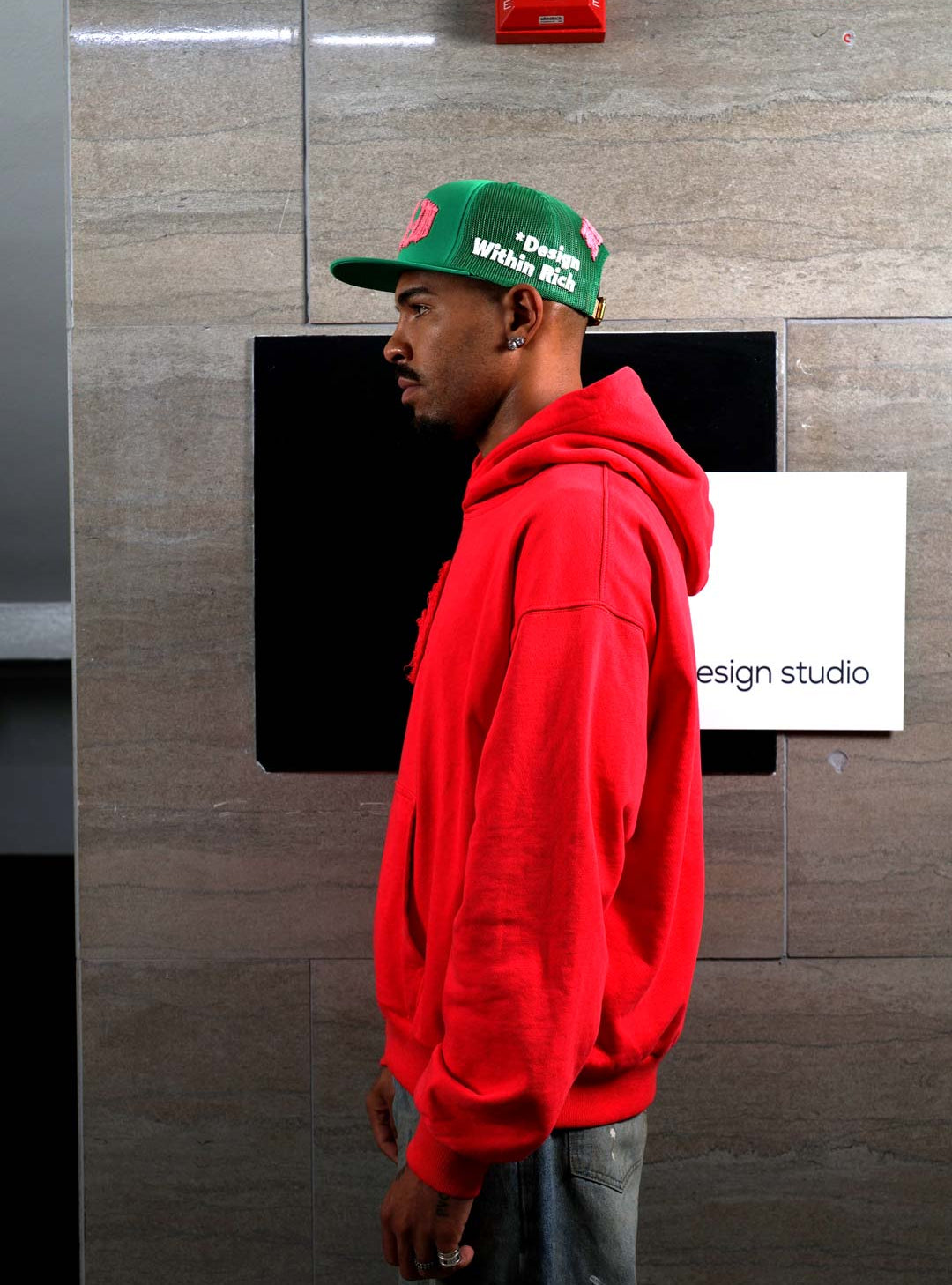 Man in red hoodie and green cap, side profile.