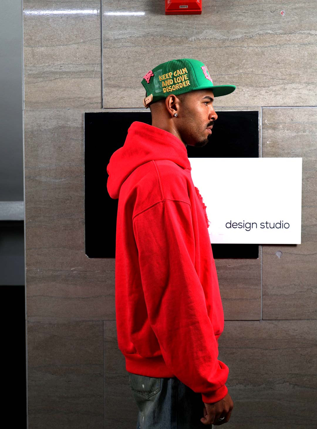 Man in red hoodie and cap, side profile.