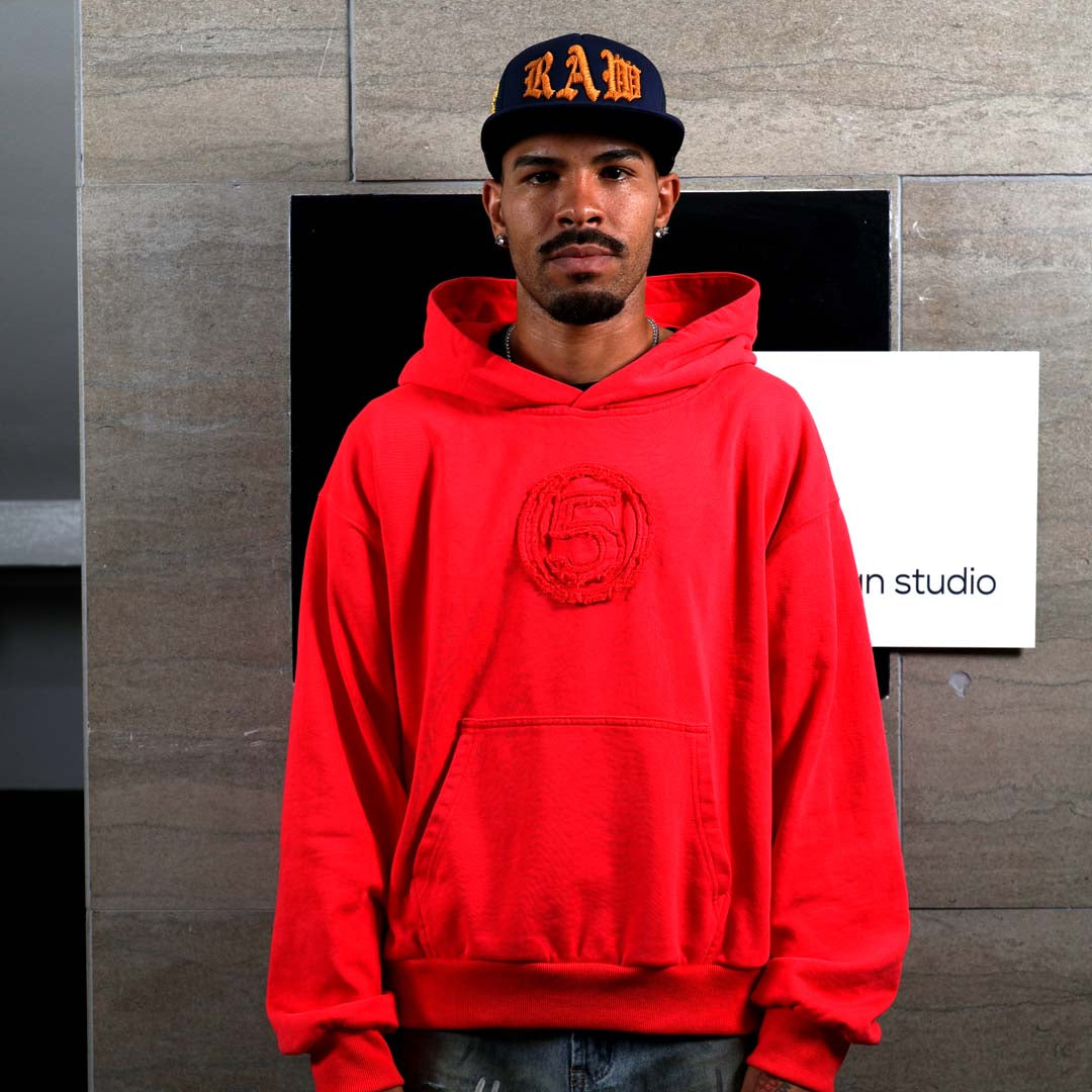 Man in red hoodie and cap standing indoors.