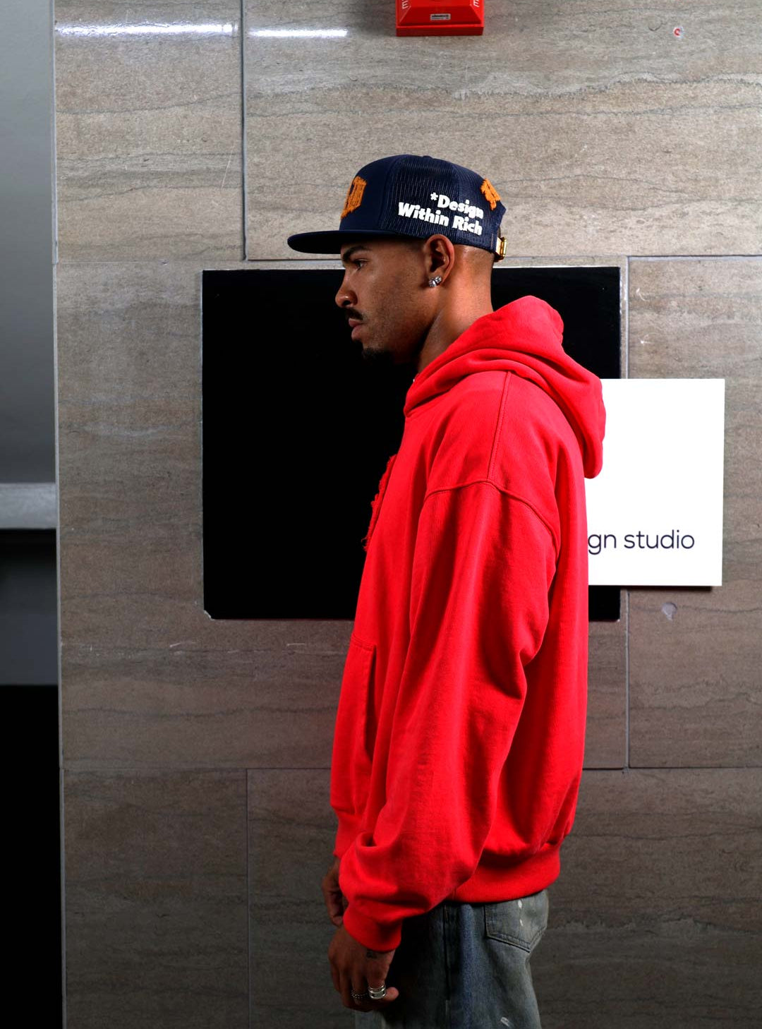 Man in red hoodie and cap, side profile.