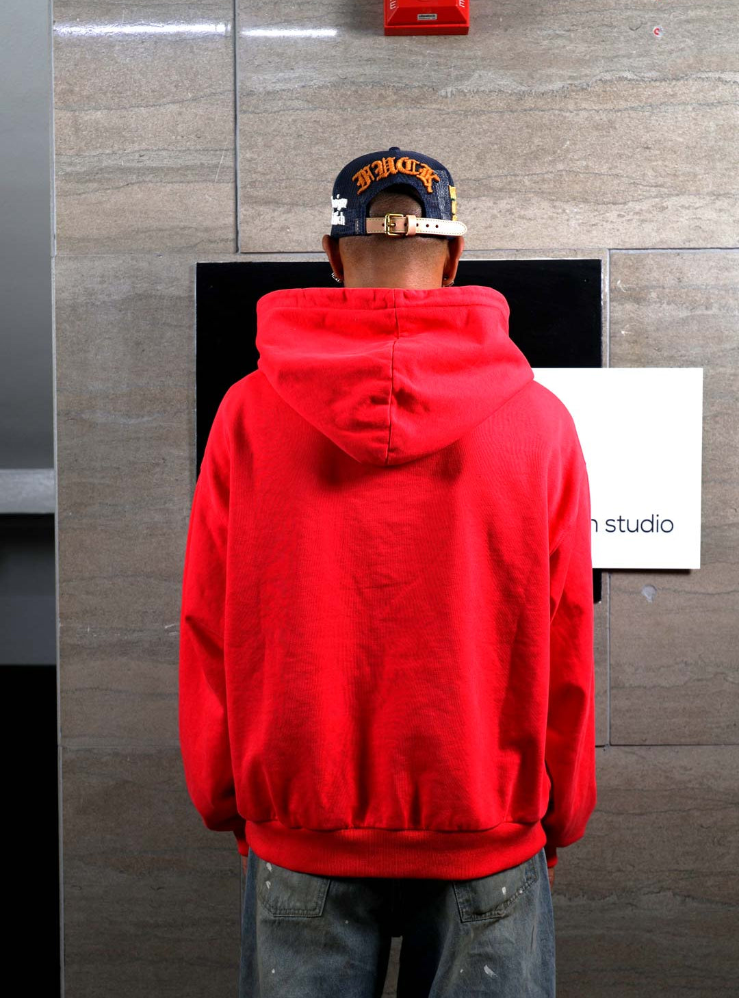 Person in red hoodie facing wall.