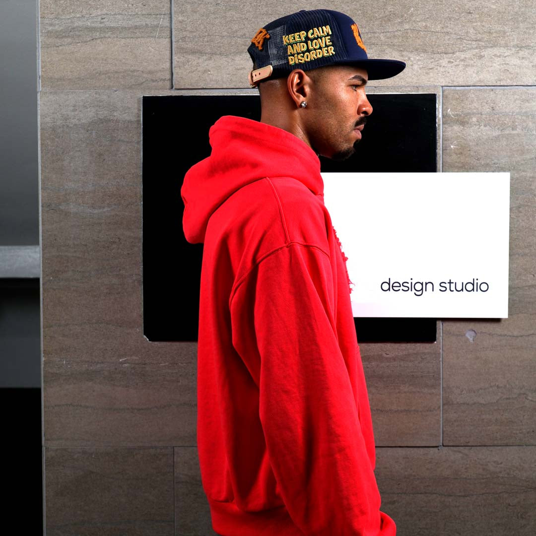 Man in red hoodie and cap near design studio sign.