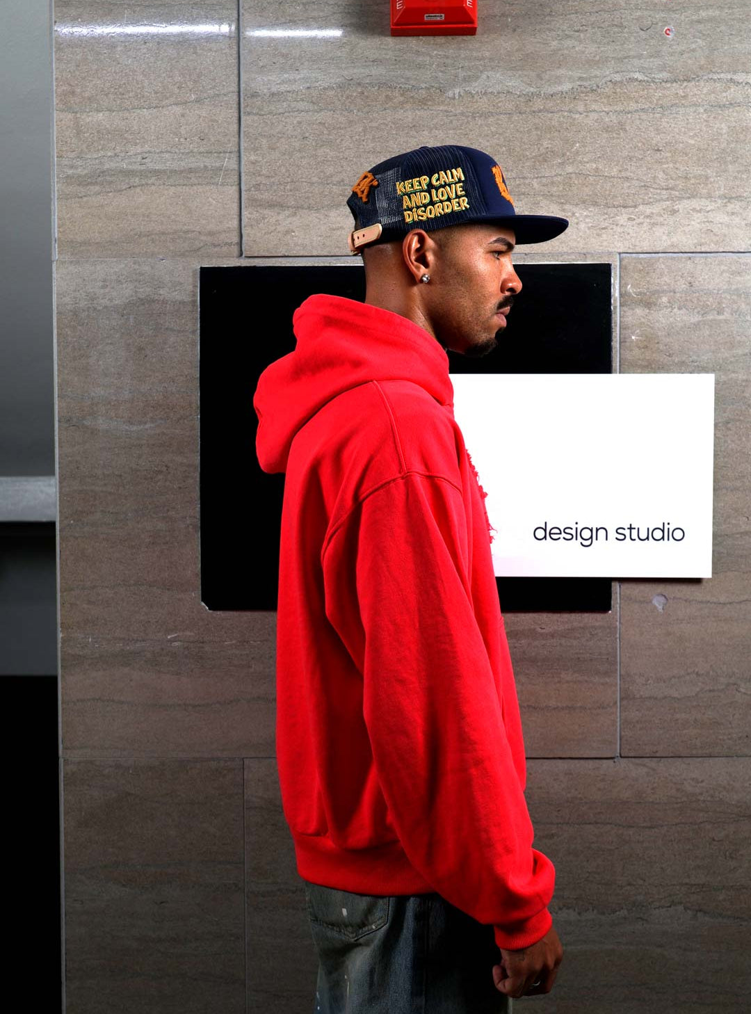 Man in red hoodie and cap near design studio sign.