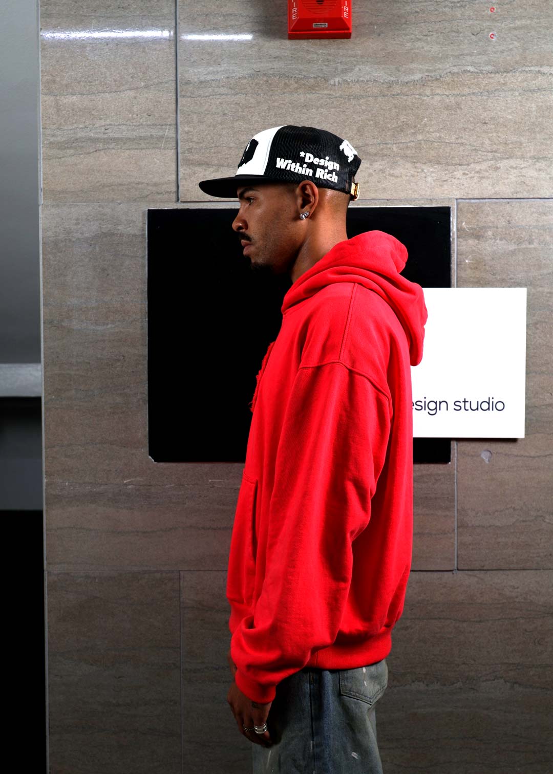 Man in red hoodie and cap, side profile.