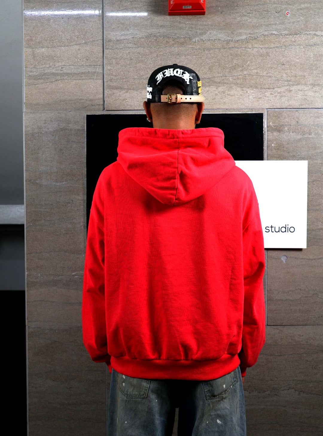 Person in red hoodie facing wall.