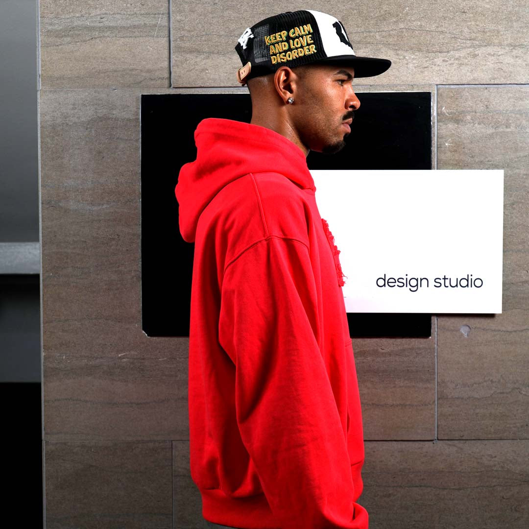 Man in red hoodie near design studio sign.