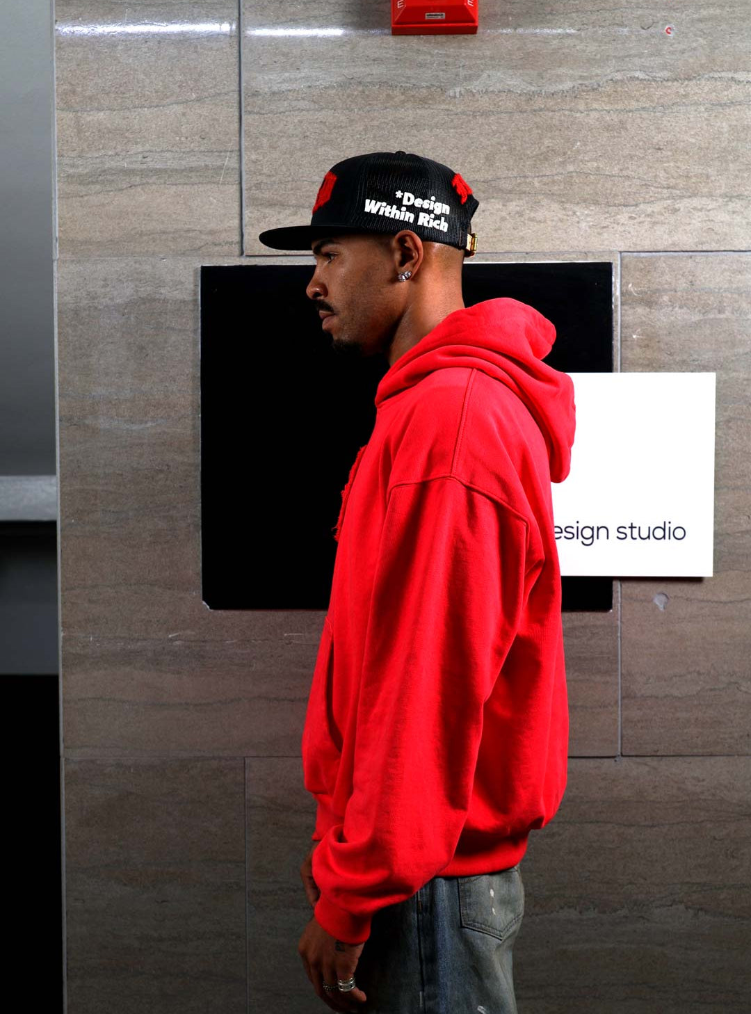 Man in red hoodie and cap, side profile.