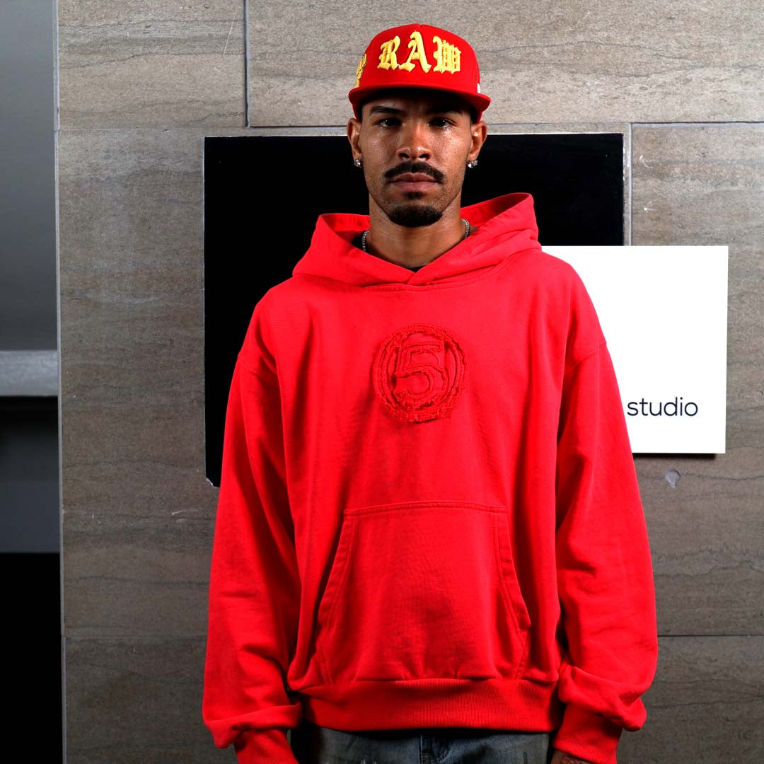 Man in red hoodie and cap standing indoors.