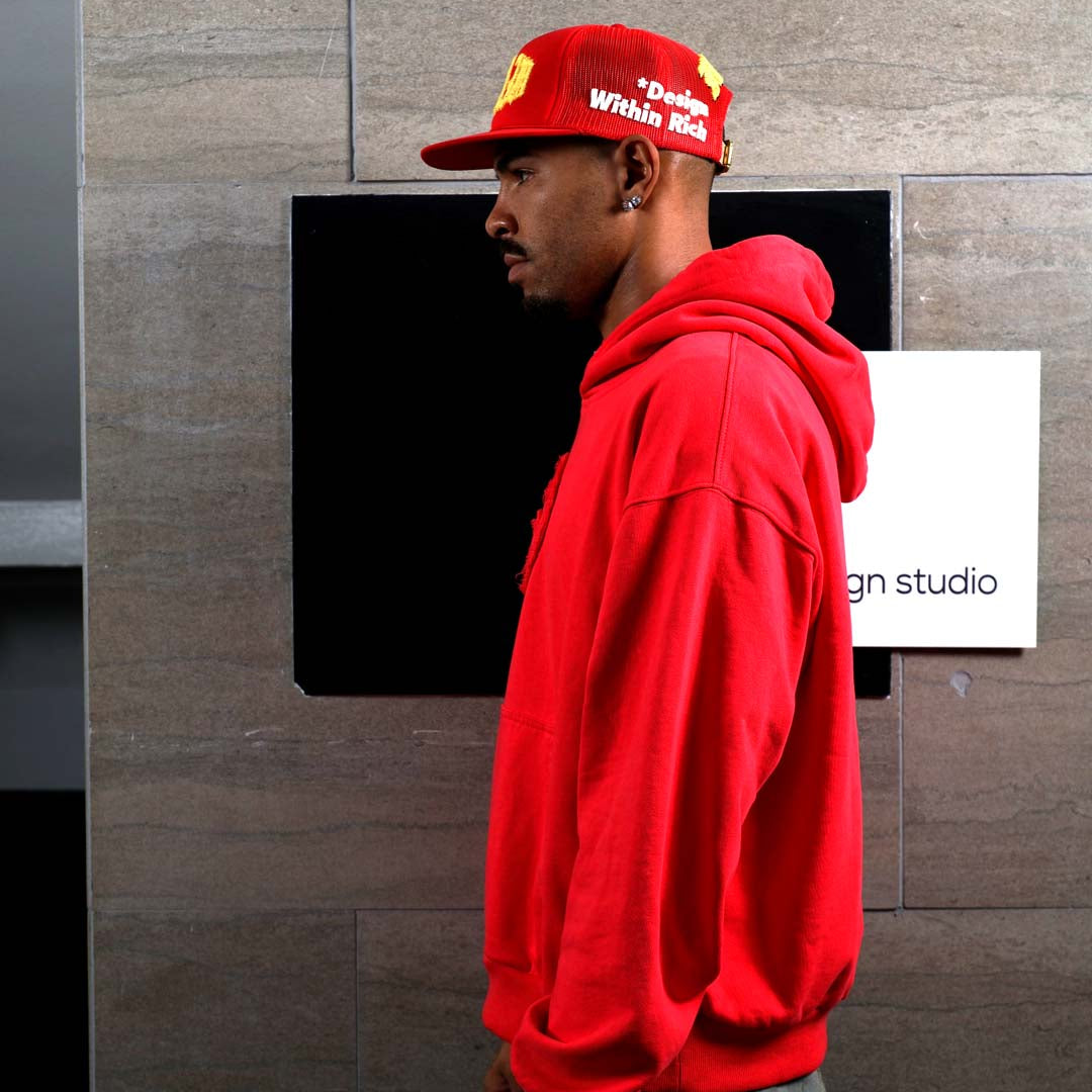 Man in red hoodie and cap, side profile.