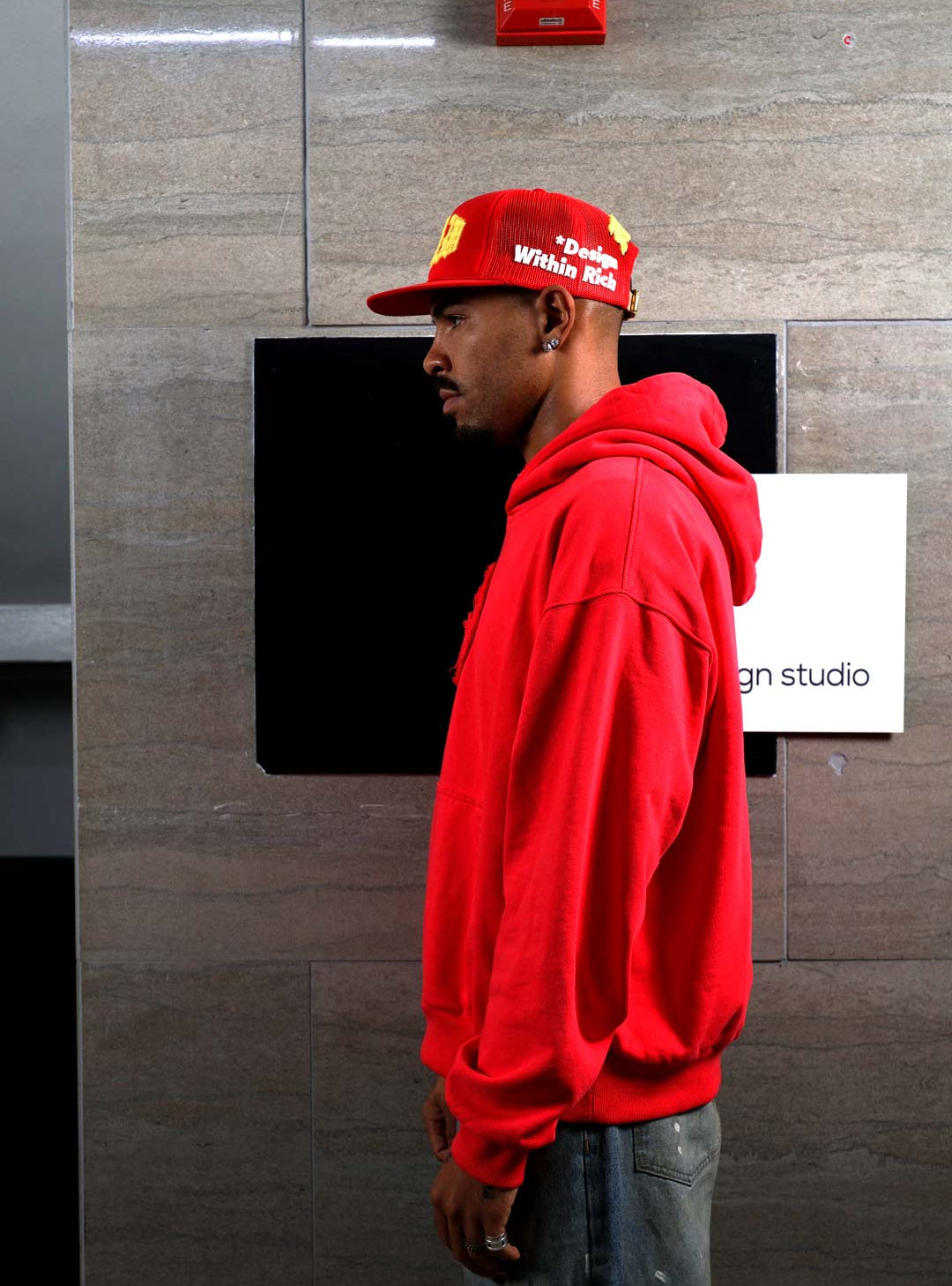Man in red hoodie and cap, side profile.
