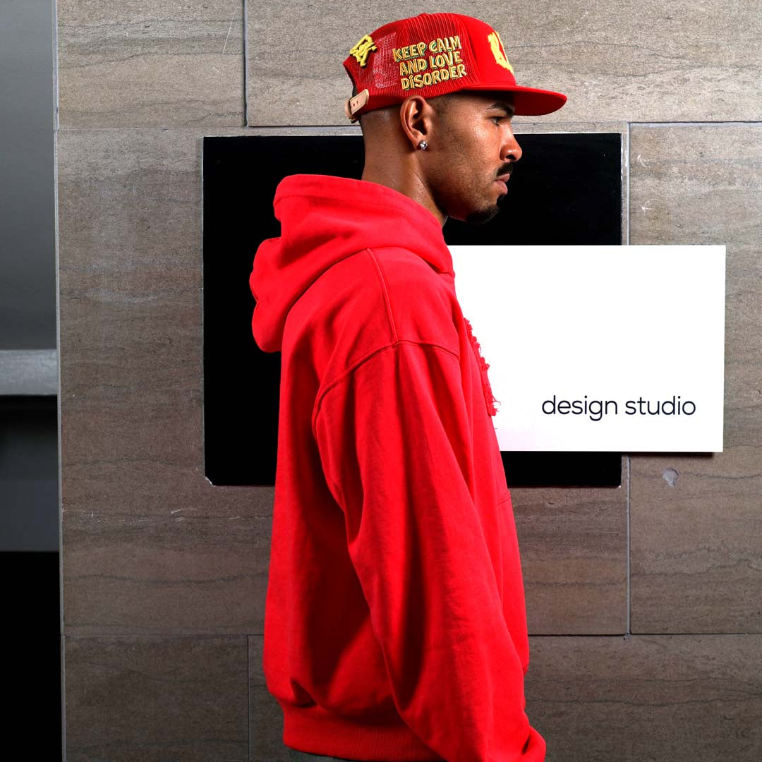 Man in red hoodie and cap near design studio sign.