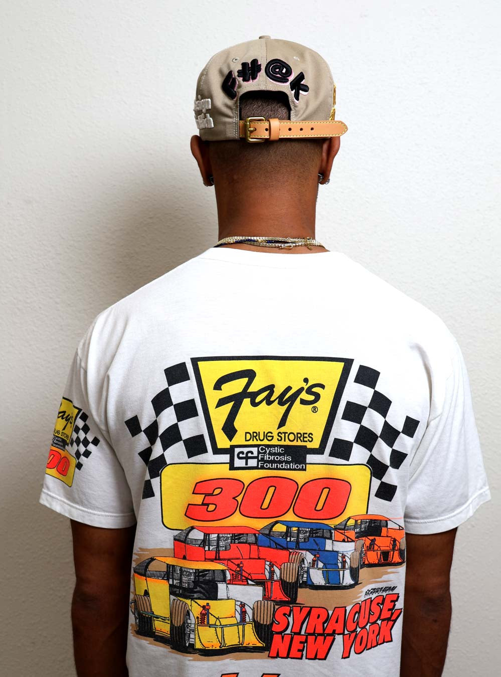 Man wearing racing-themed shirt and cap, back view.