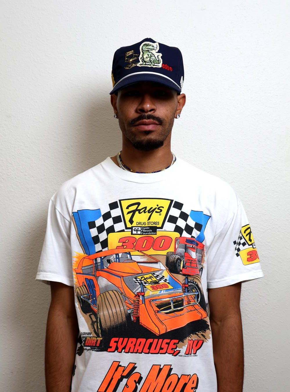 Man wearing racing-themed shirt and cap.
