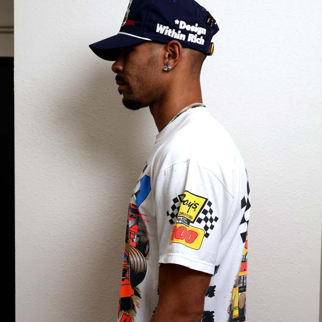 Man in graphic t-shirt and cap, side view.