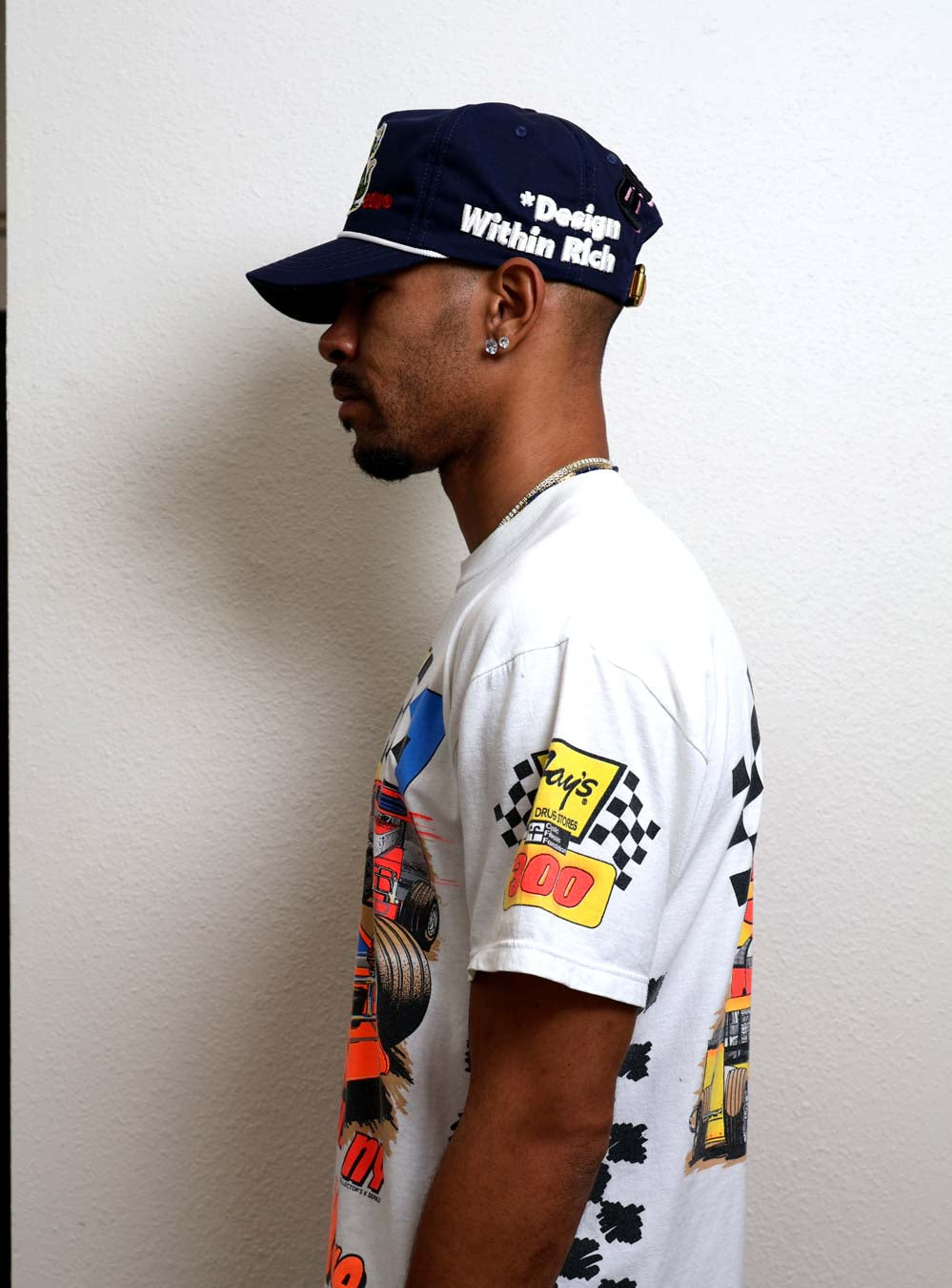 Man in graphic t-shirt and cap, side view.