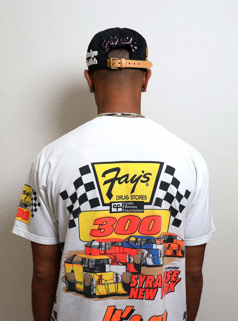Man wearing graphic racing-themed shirt and cap.