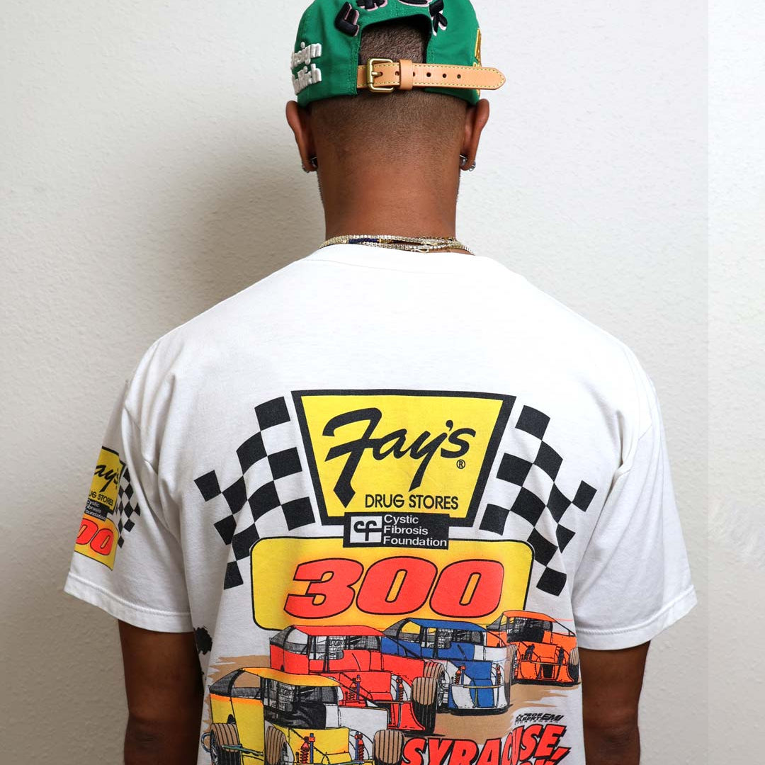 Man wearing racing-themed shirt and green cap.