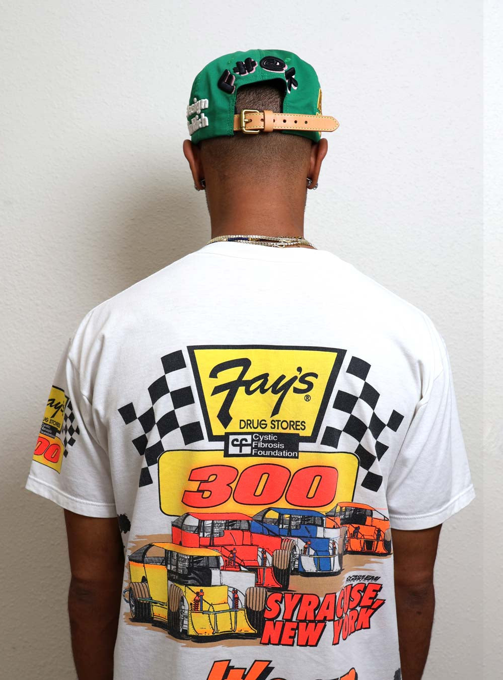 Man wearing racing-themed shirt and green cap.