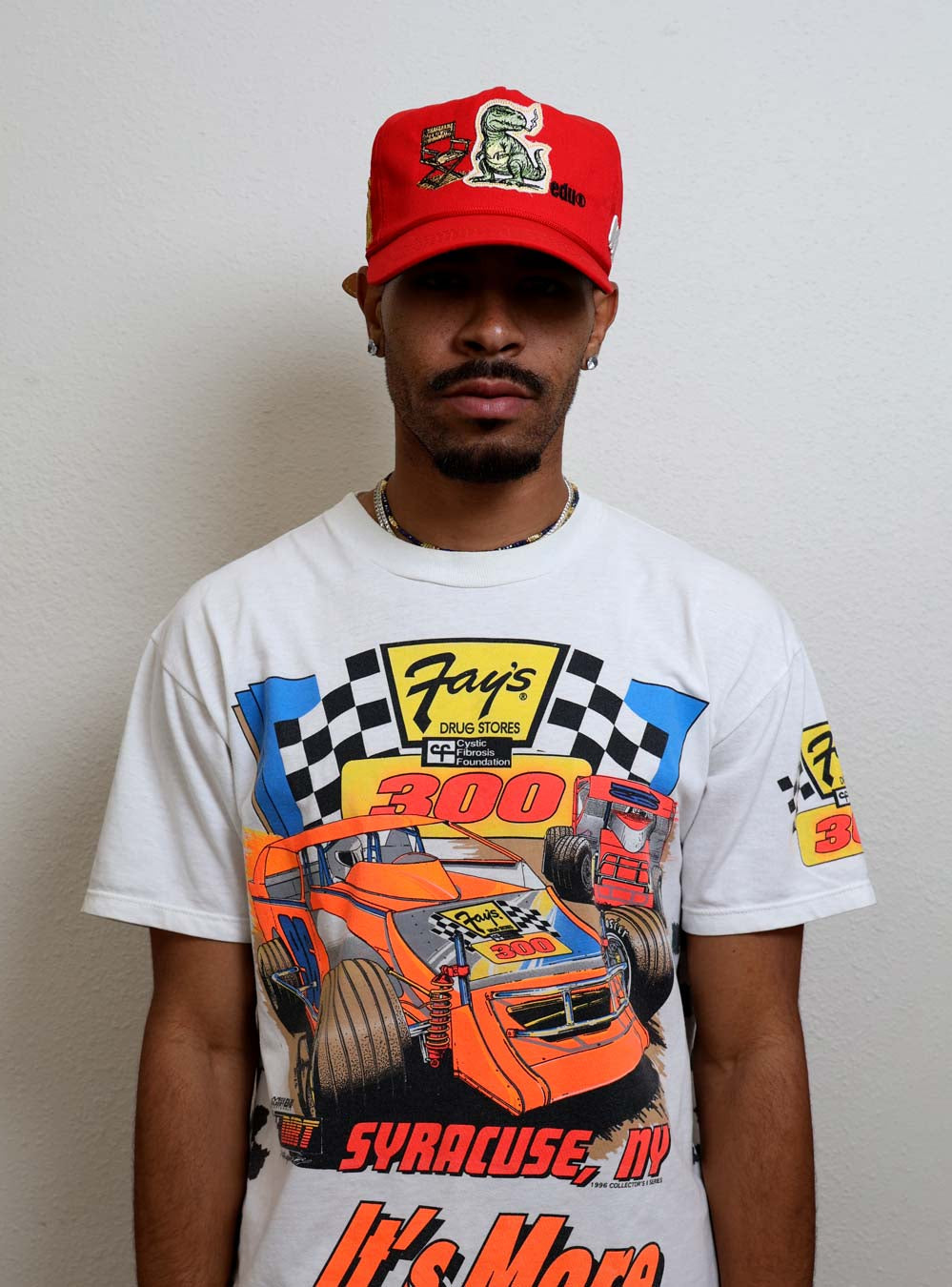 Man wearing racing-themed shirt and red cap.