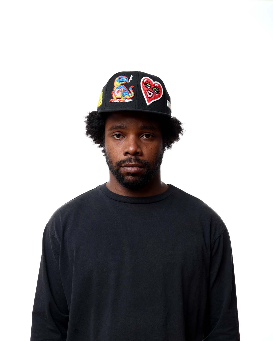 Person wearing a black cap with colorful designs on a white background