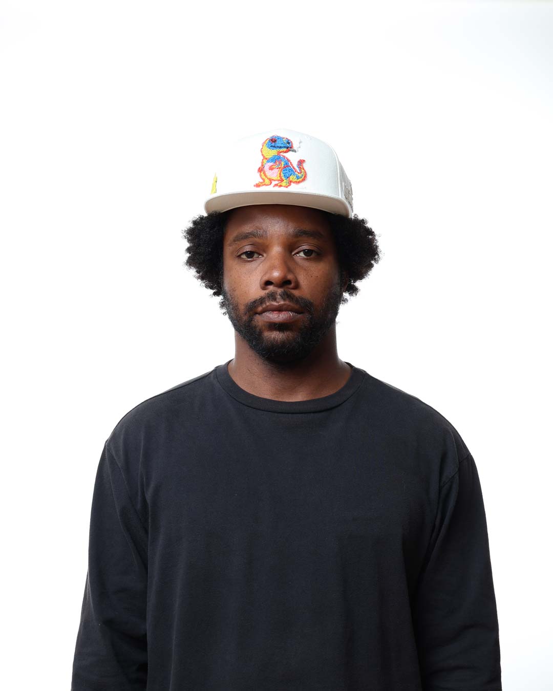 Man wearing a black long-sleeve shirt and a white cap with colorful design on a white background