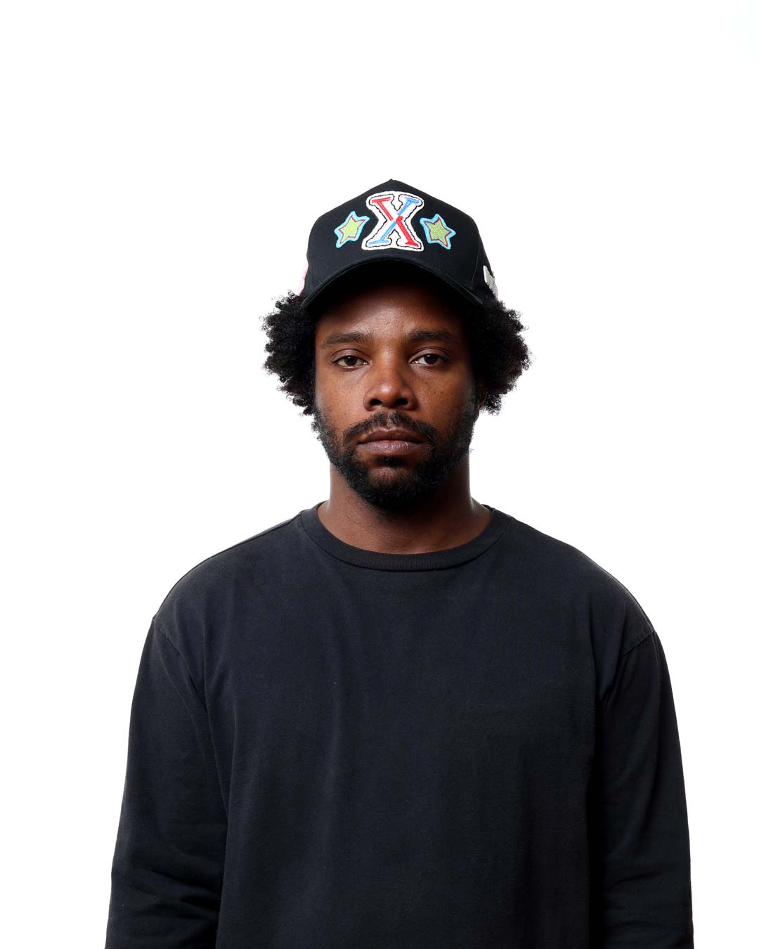 Man wearing a black cap with colorful designs on a white background