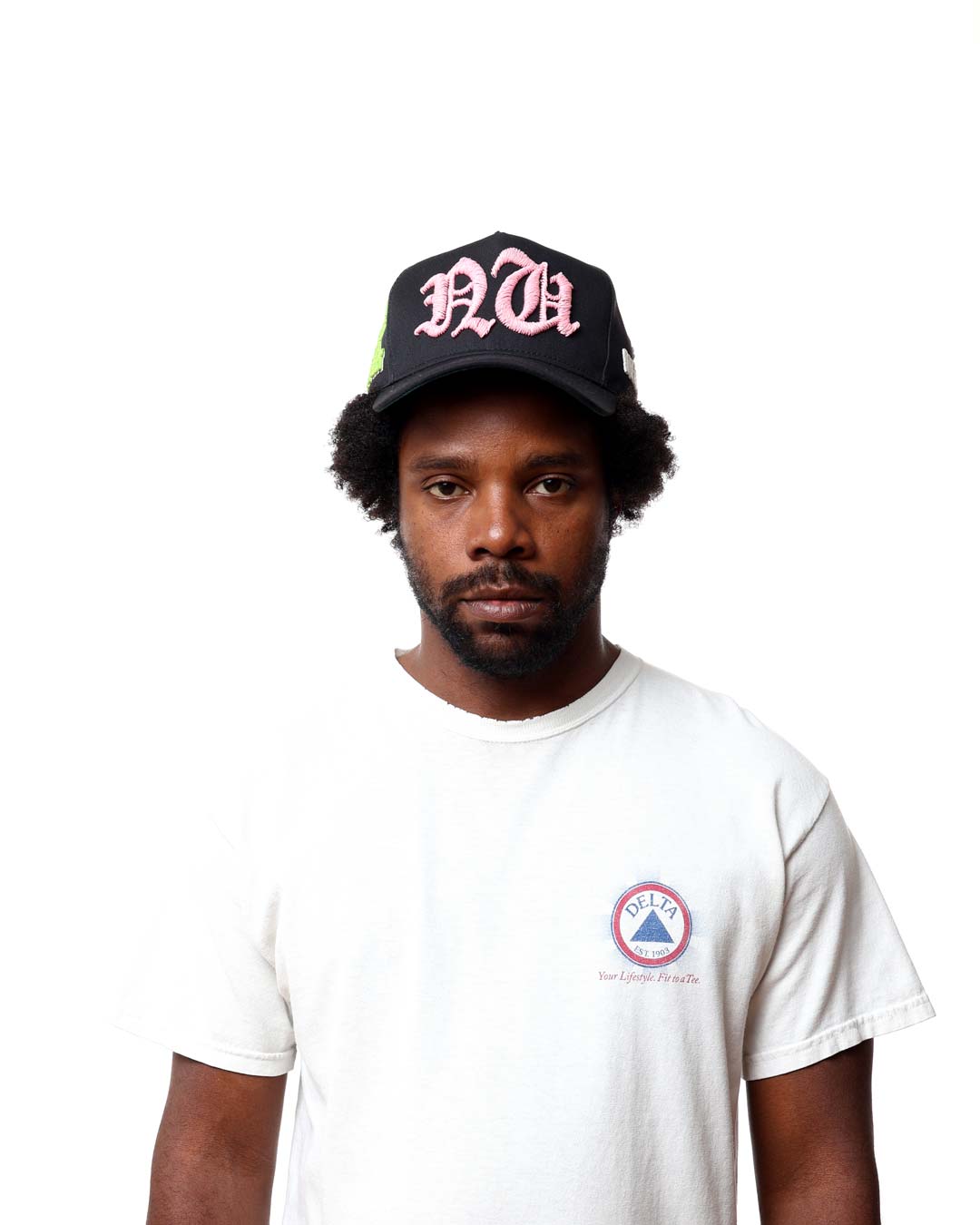 Man wearing a black cap with pink text and a white t-shirt with a logo on a white background