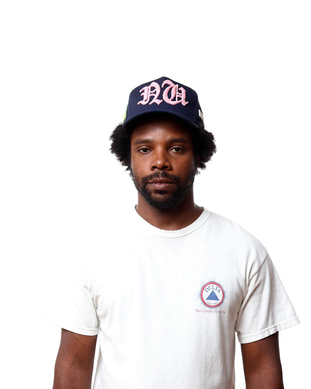 Man wearing a navy cap with pink text and a white t-shirt with a logo on a white background