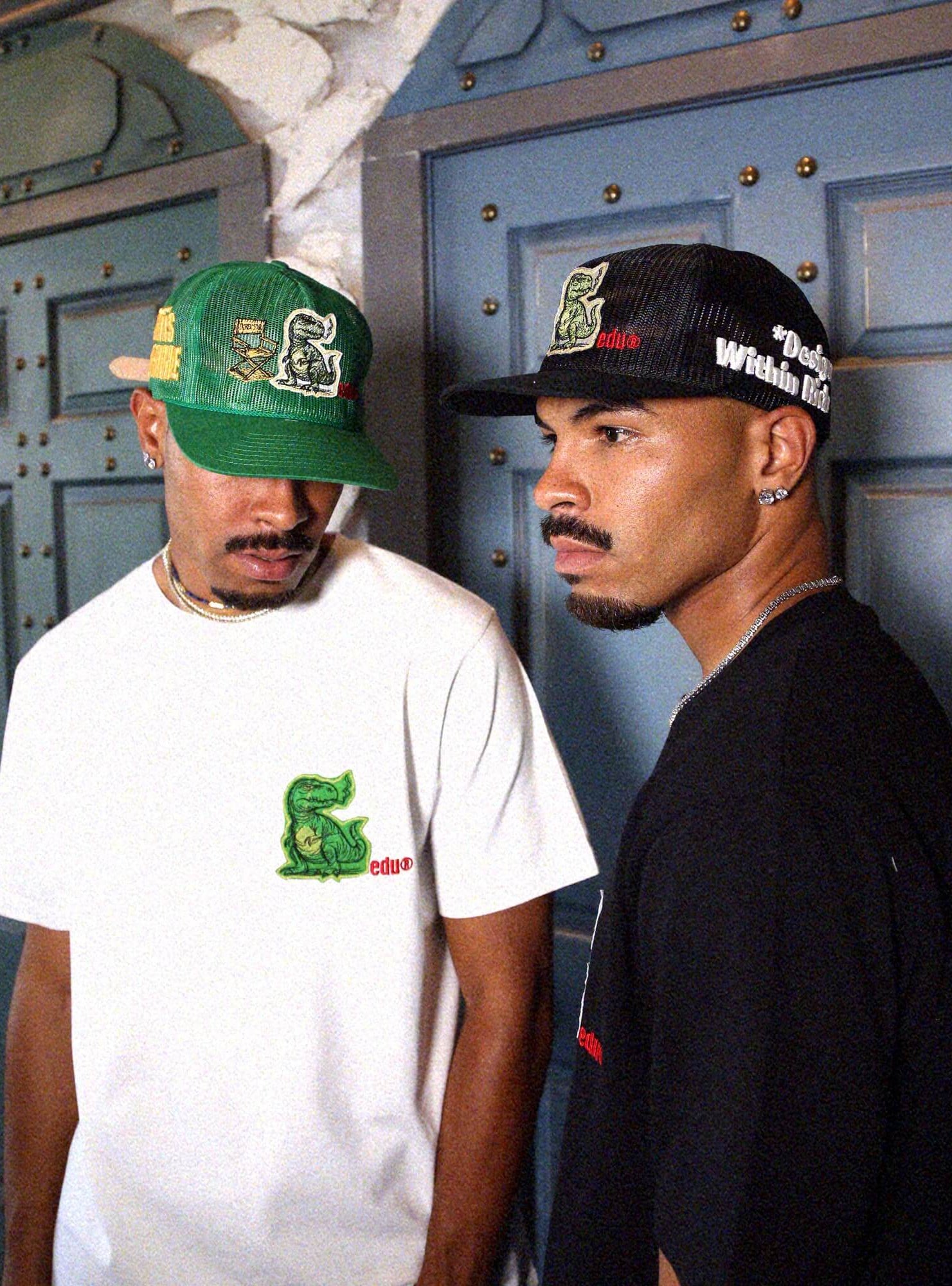 Two men in graphic t-shirts and embroidered caps.