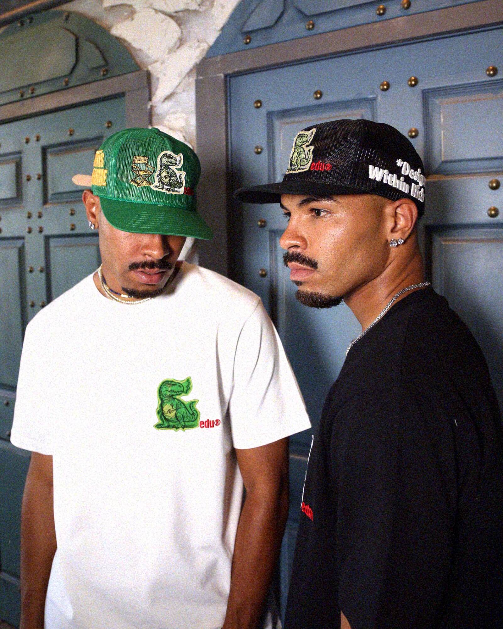 Two men in graphic t-shirts and embroidered caps.