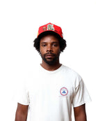 Man wearing a red cap and white t-shirt with a logo on a white background