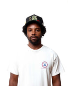 Man wearing a white t-shirt with a logo and a black cap on a white background